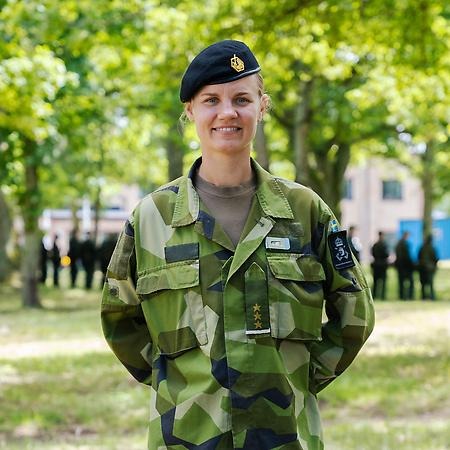 Kvinna i militärkläder med träd i bakgrunden. 